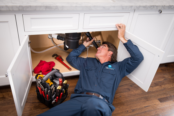 The Brisbane Plumbers technician repairing under-sink plumbing and garbage disposal in a Brisbane kitchen