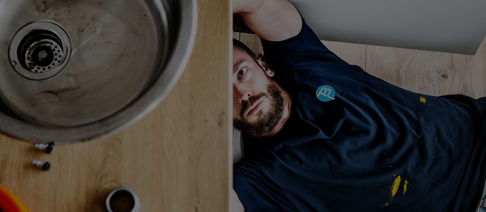 Licensed plumber lying under a kitchen cabinet inspecting sink drain fittings and pipework in Brisbane