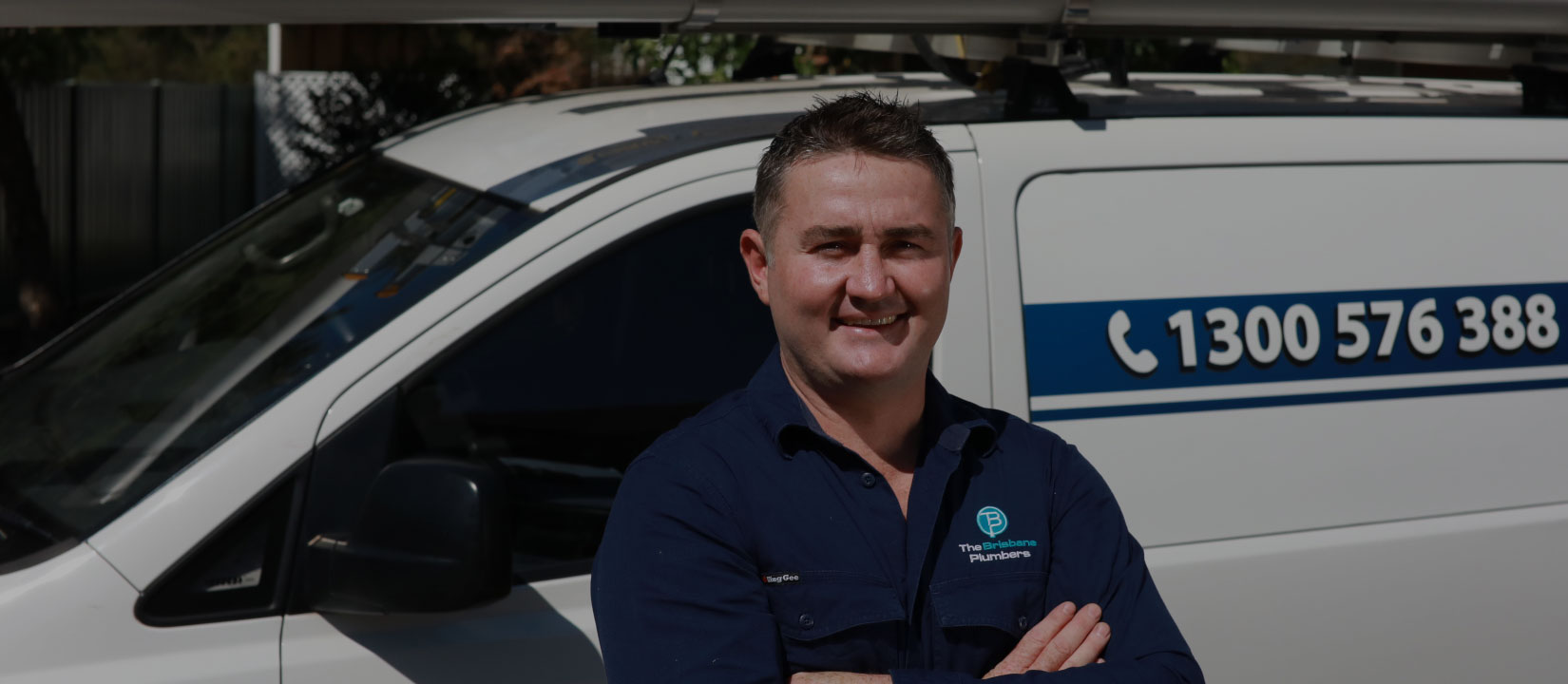 Joseph, Director of The Brisbane Plumbers, standing confidently in front of the service van displaying 1300 576 388