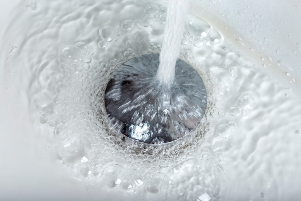 Water flowing down a bathroom sink drain with visible bubbles and running tap water