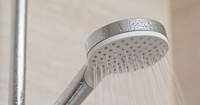 Shower head running with water spraying evenly in a bathroom