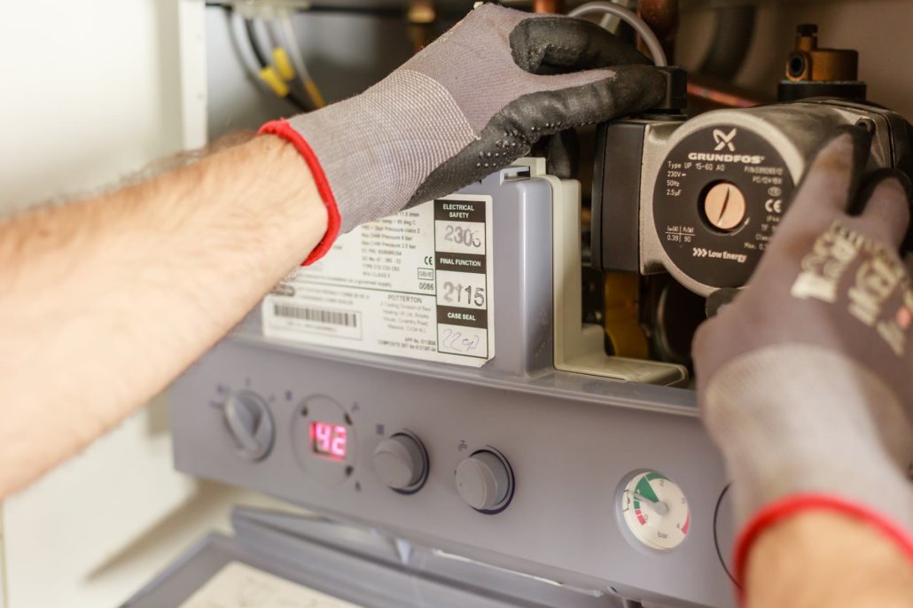 Plumber adjusting a residential boiler and circulation pump during hot water system maintenance