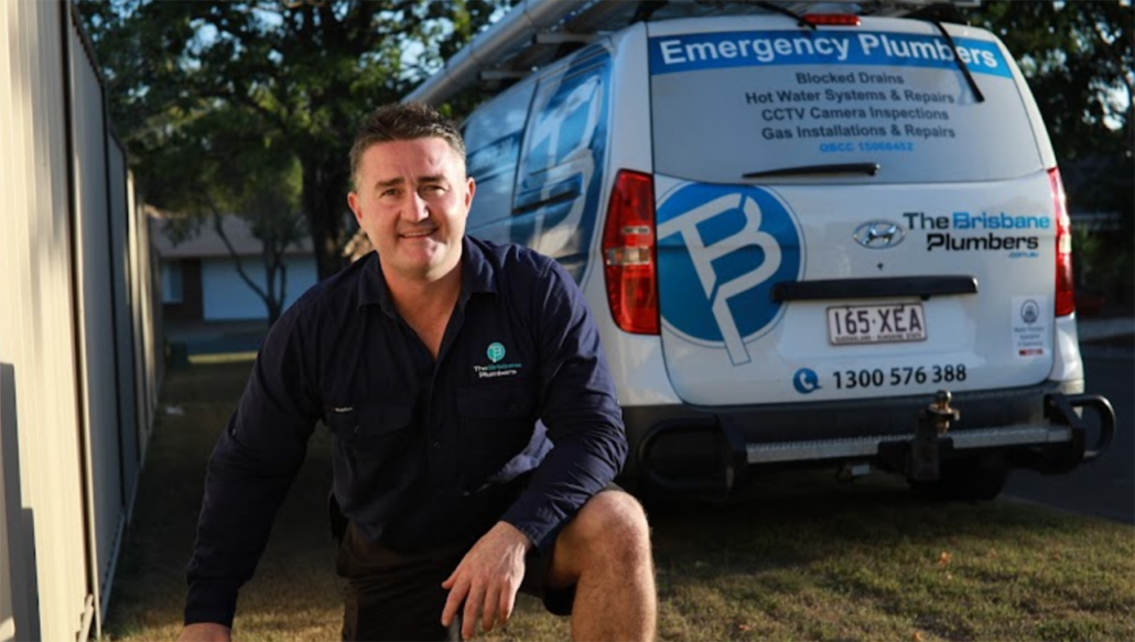Joseph from The Brisbane Plumbers kneeling in front of an emergency plumbing service van in Brisbane