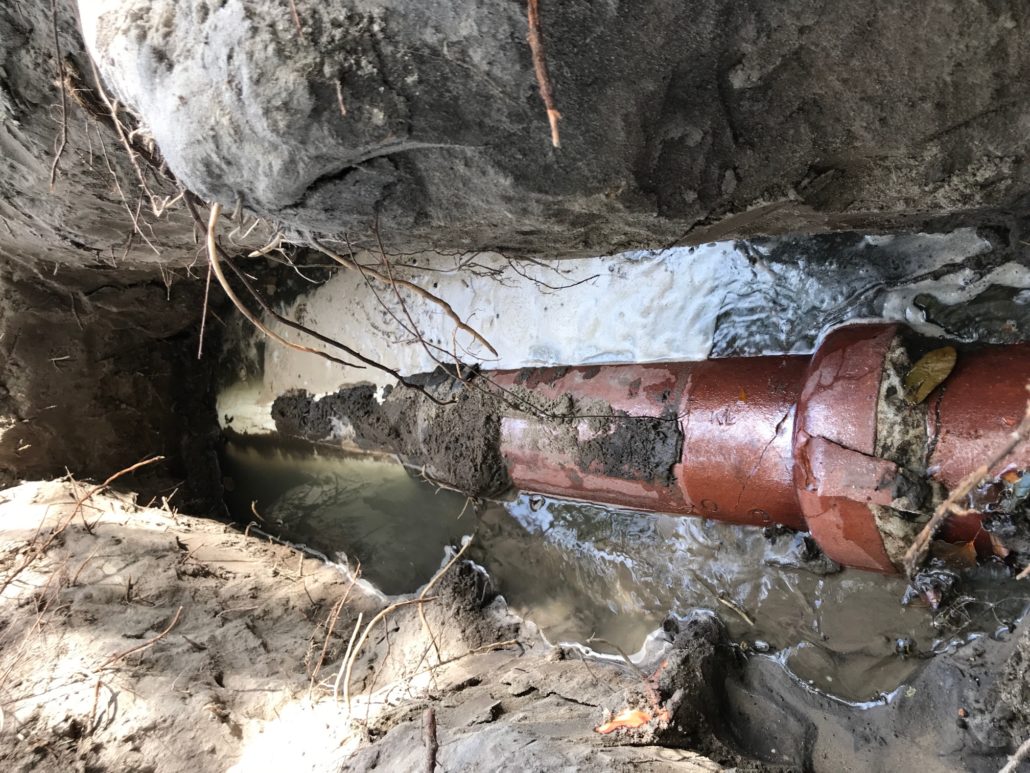 Damaged underground sewer pipe with visible crack and water leakage in an excavated trench