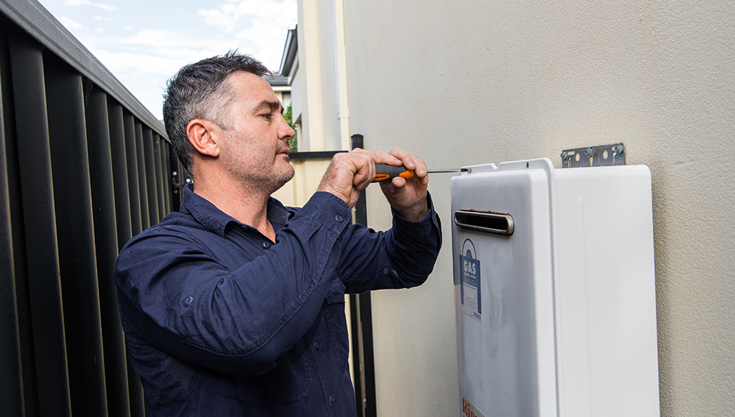 Licensed Brisbane plumber servicing an outdoor gas hot water system mounted on a residential wall