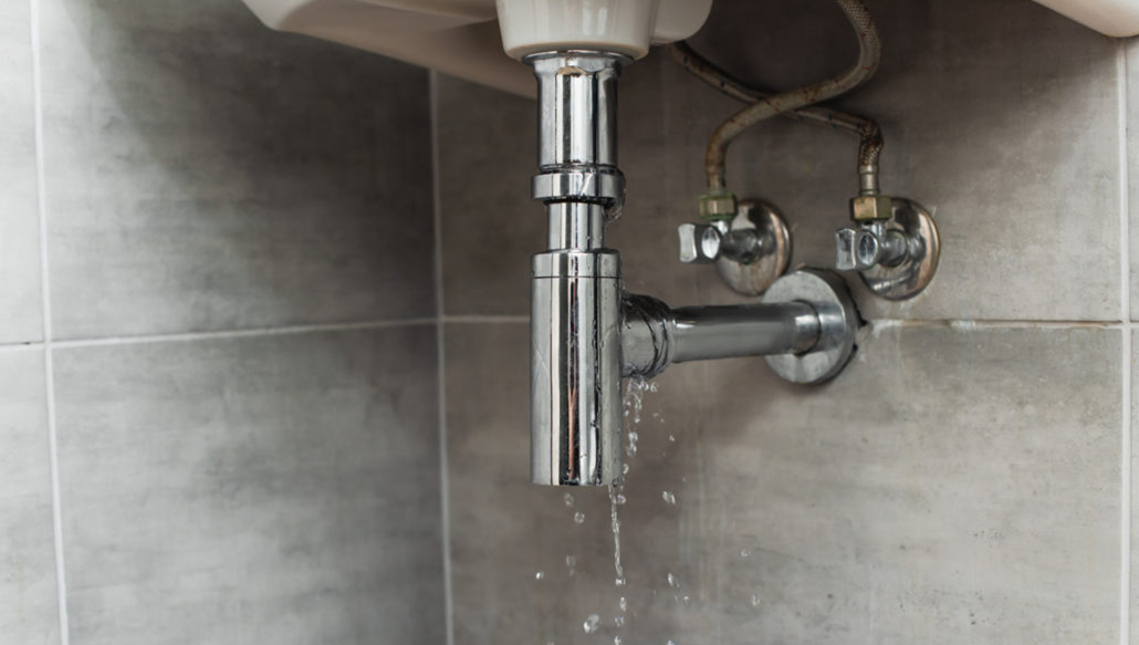 Leaking bathroom sink pipe and drain trap with water dripping underneath the basin
