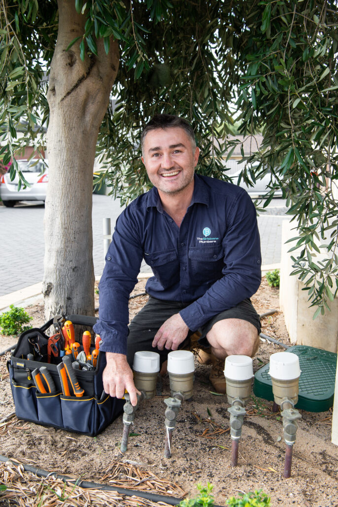 Brisbane plumber inspecting residential water meter connections and shutoff valves outdoors