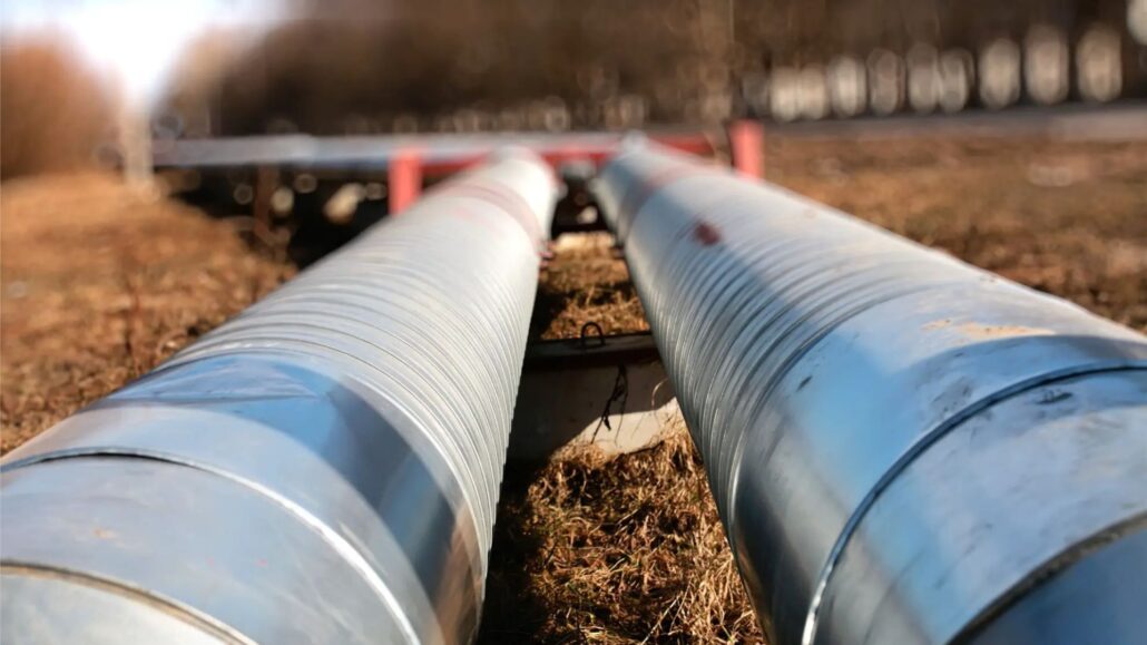 A close-up view of two long metal pipes on the ground, positioned parallel to each other with a blurry background.