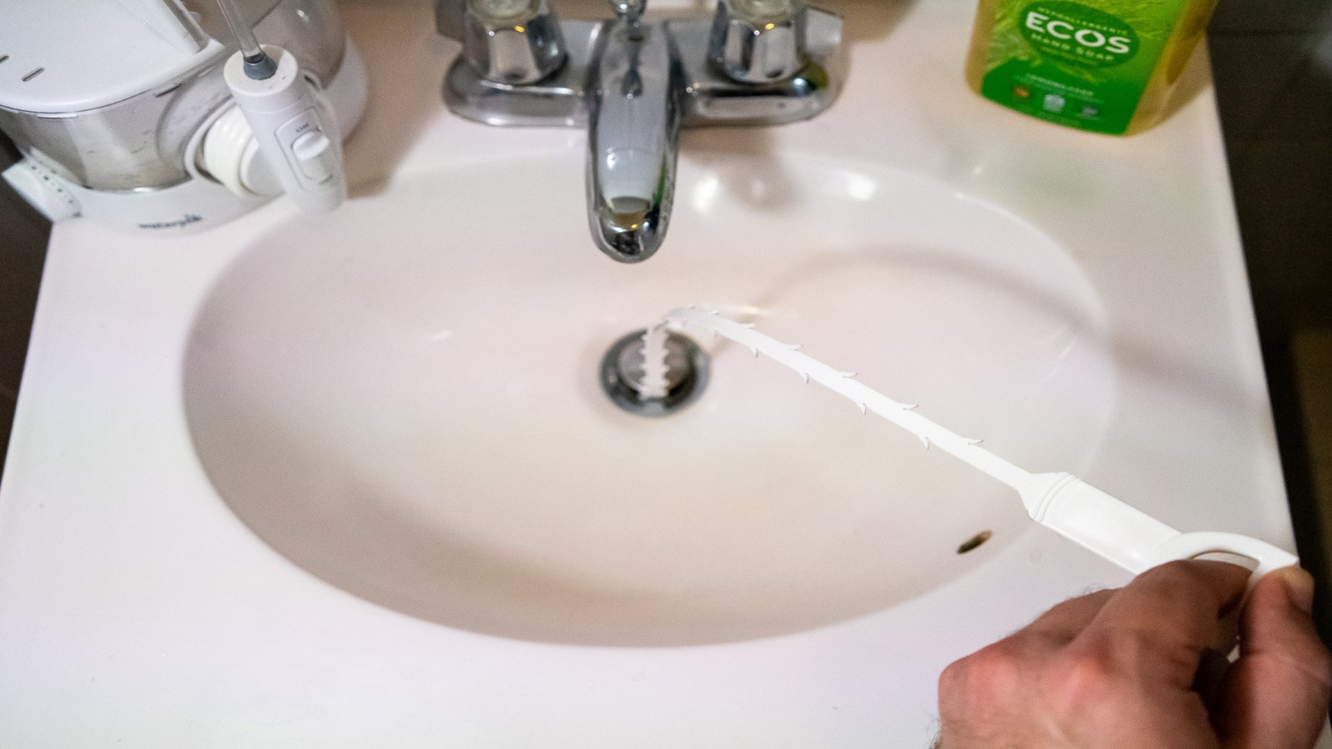 Plumber clearing a blocked bathroom sink drain with a drain snake tool in Brisbane