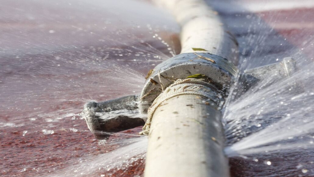 A close-up image of a cracked water pipe, with water spraying out forcefully from the break, creating multiple streams of water.