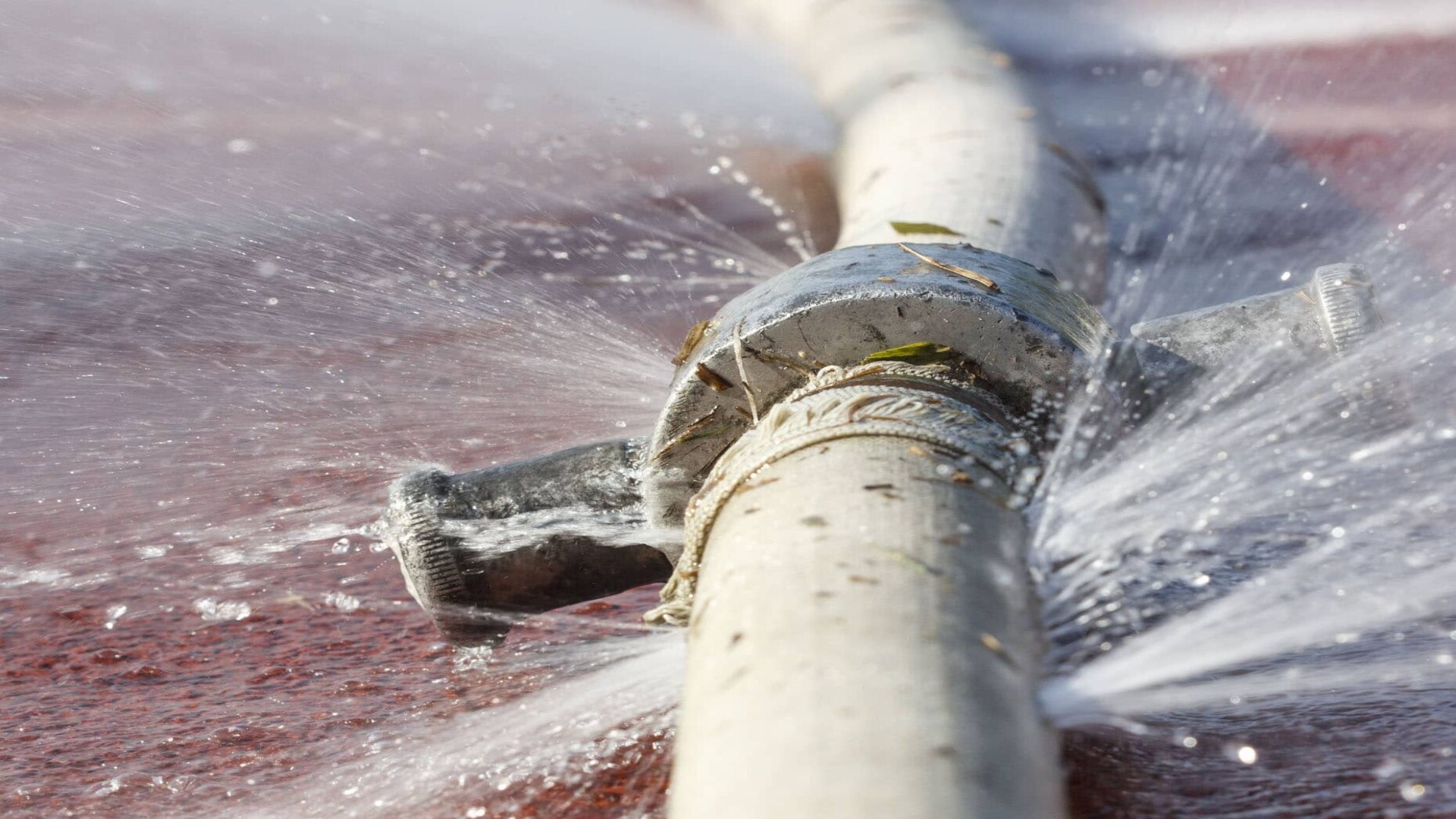 A close-up image of a cracked water pipe, with water spraying out forcefully from the break, creating multiple streams of water.