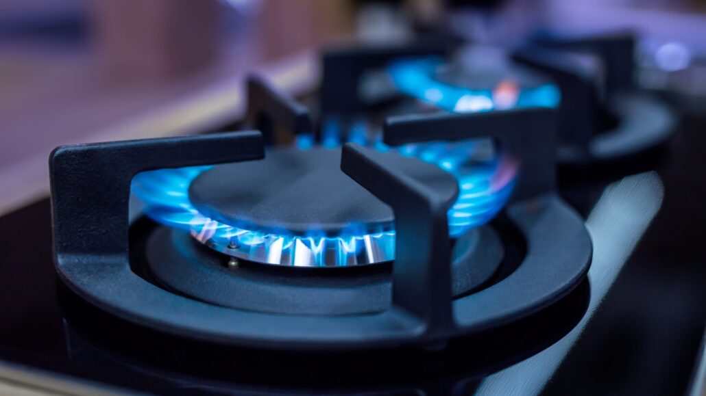 Close-up of a gas burner with blue flames igniting on a stovetop.