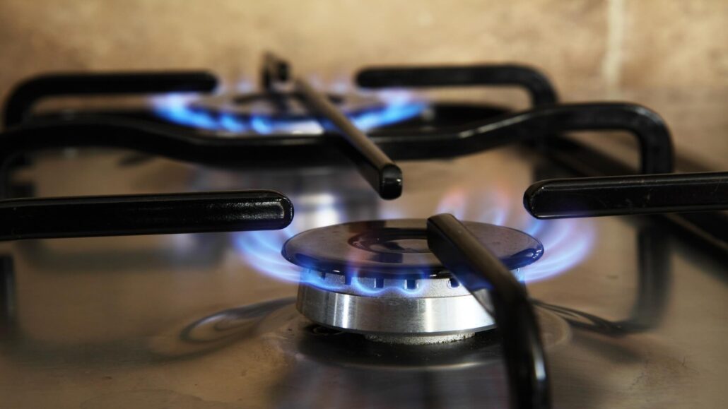 A close-up view of a gas stove with blue flames coming from one of the burners, surrounded by black metal grates.