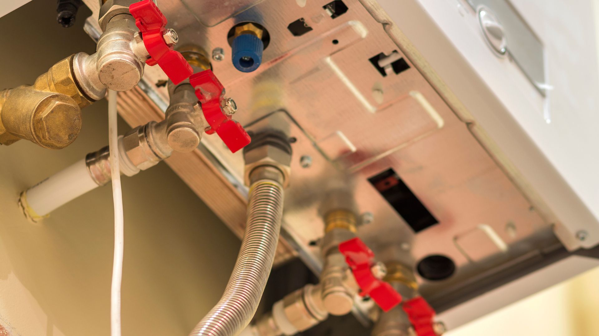 A close-up view of the plumbing system of a water heater with multiple brass valves and connections, including red valve handles.