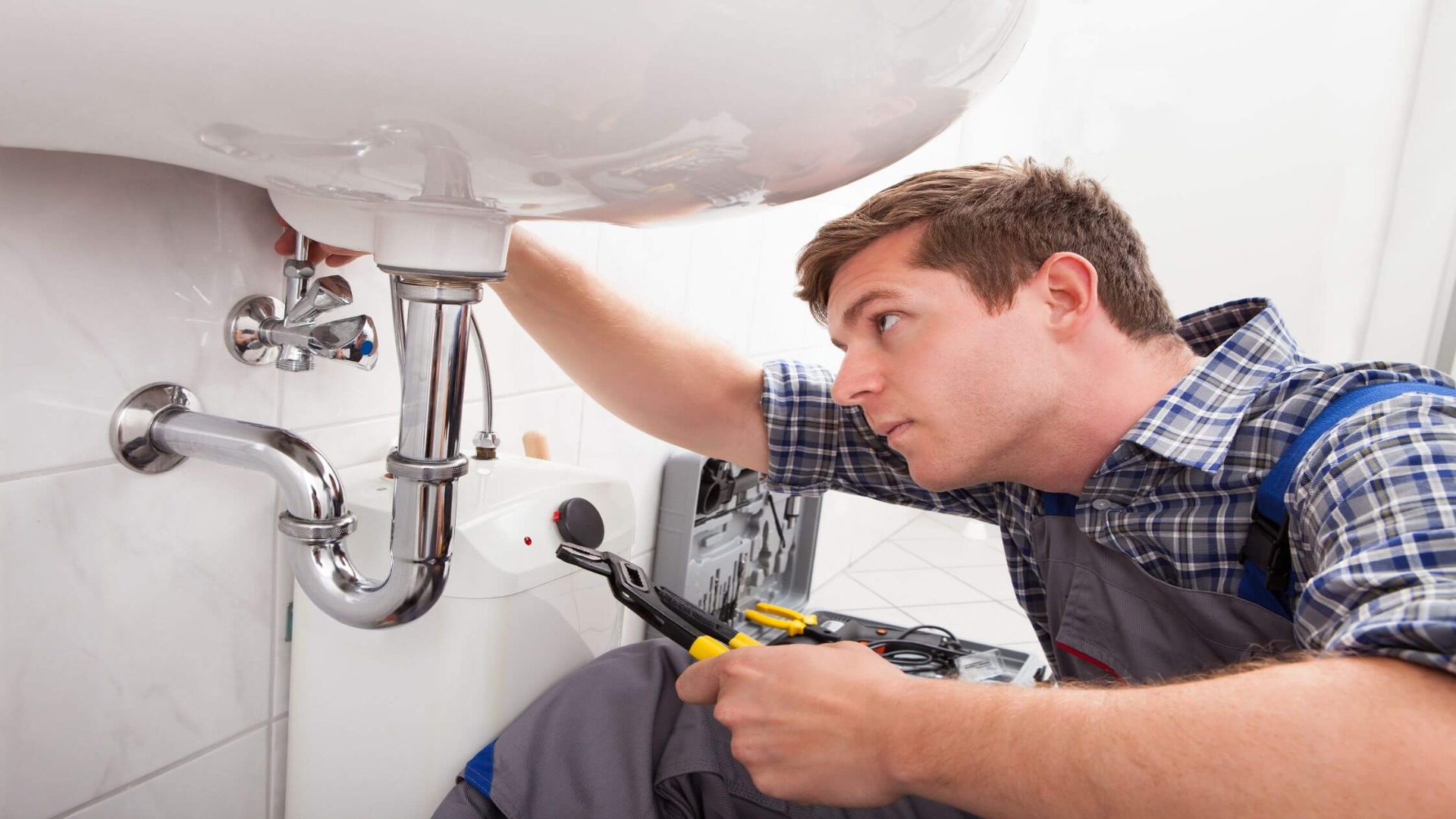 A plumber working under a sink, tightening a pipe with a wrench.