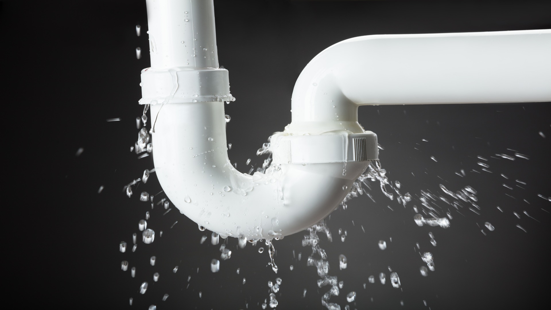 A leaking PVC pipe with water spraying out from a joint.