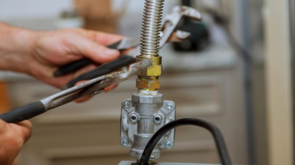 A person using pliers to tighten a metal connector on a flexible gas pipe.