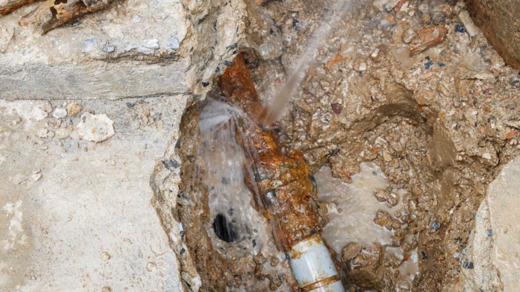 A burst water pipe leaking water with soil and debris around it.