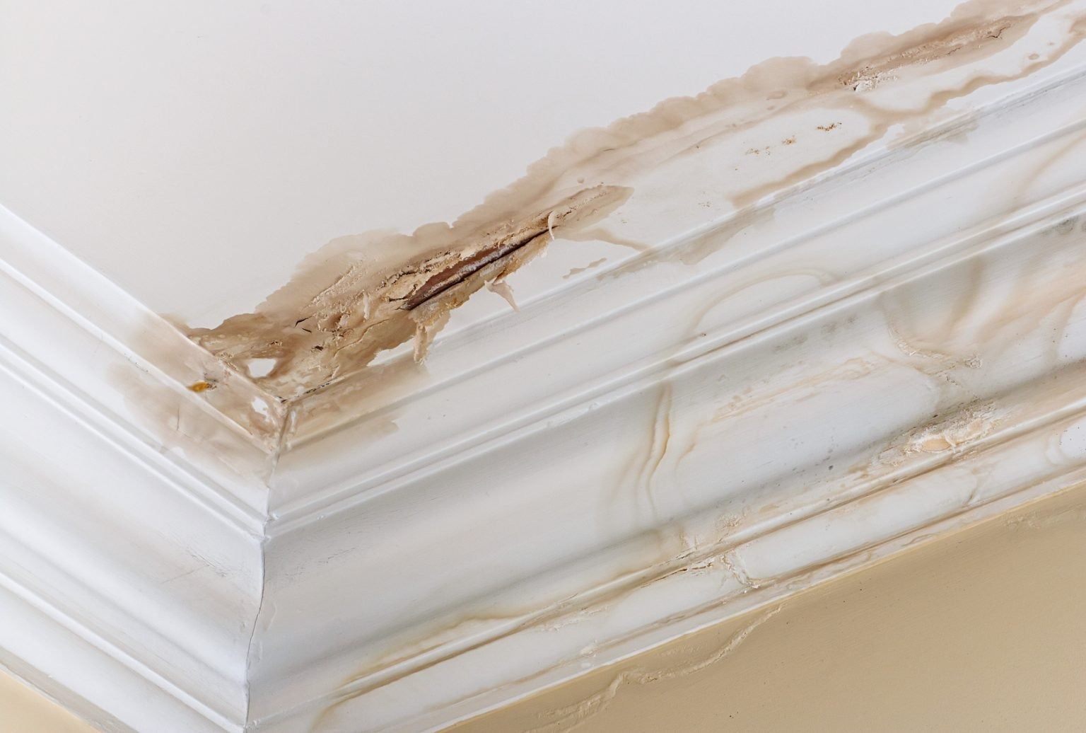 Water damage on a ceiling corner with visible stains and peeling paint, indicating a potential plumbing leak or roof leak.