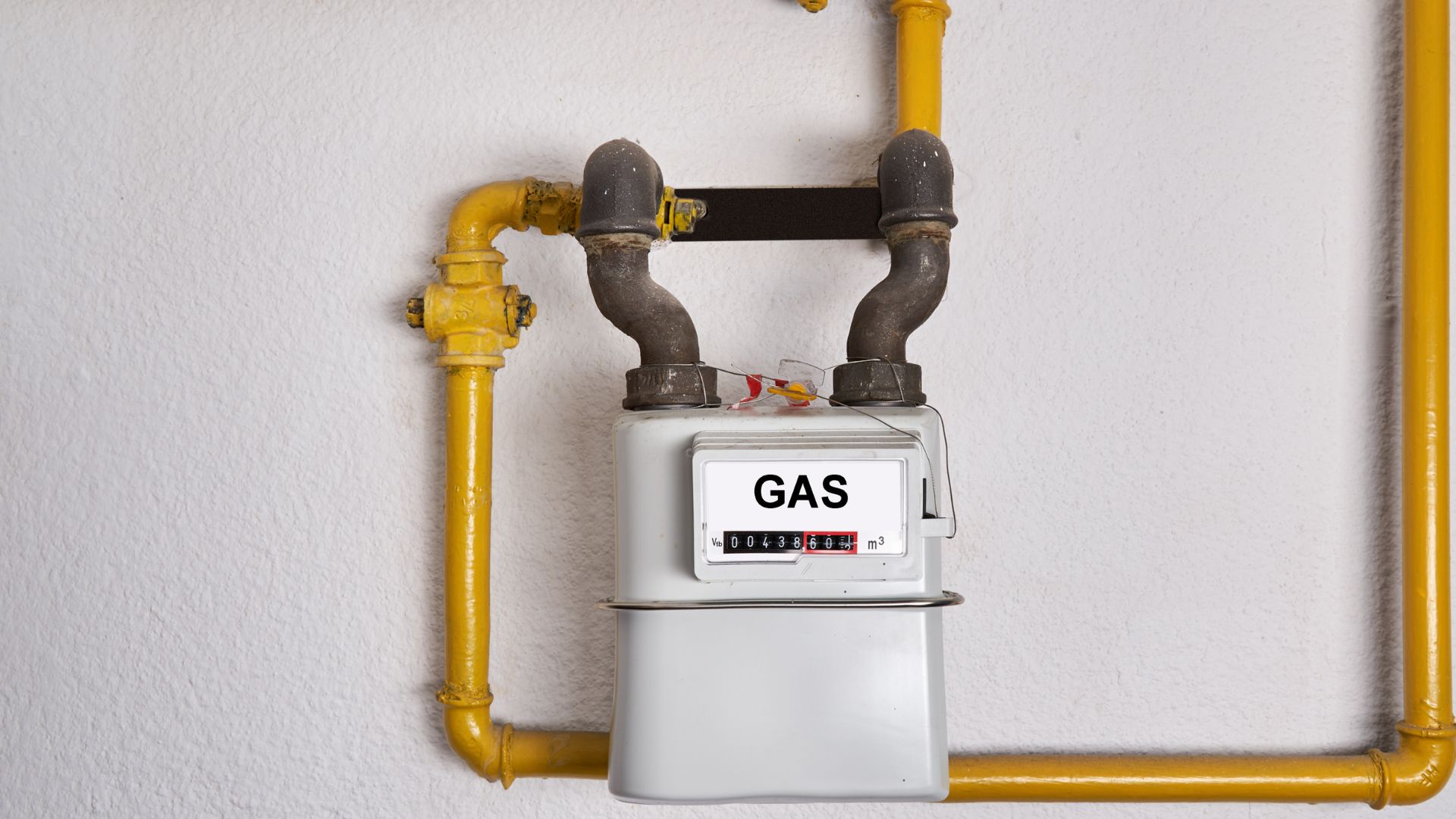 Close-up of a gas meter attached to yellow gas pipes on a wall, displaying the gas usage readings.
