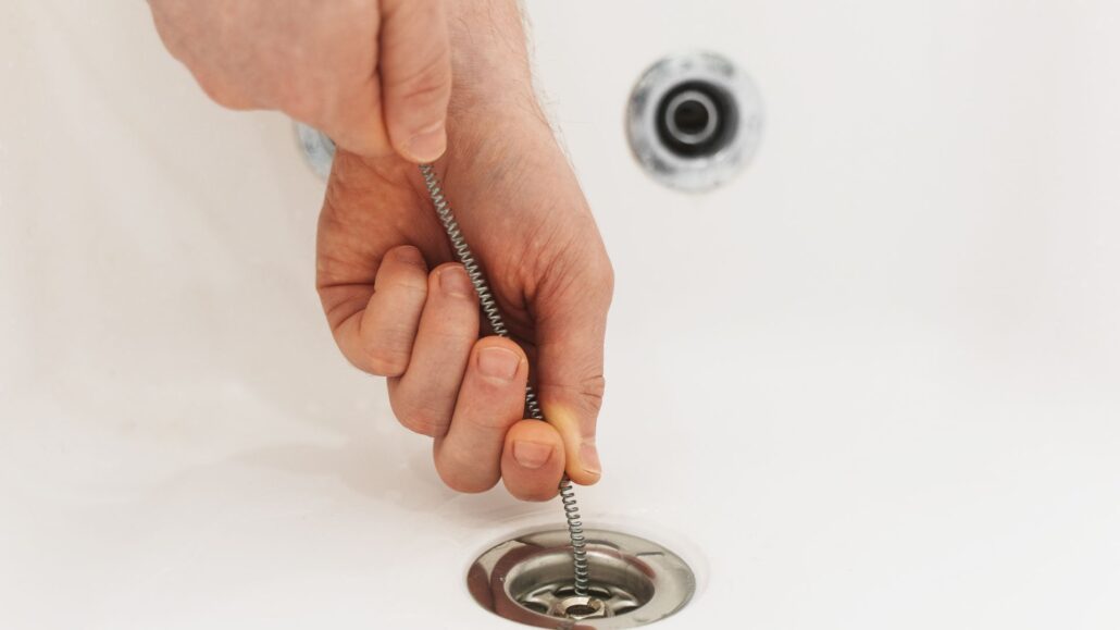 Plumber using a drain snake to clear a blocked bathtub drain in Brisbane