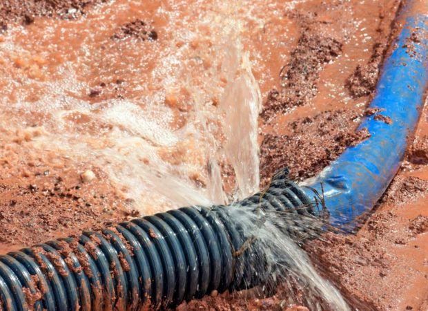 A damaged blue hose spraying water with mud around it, showing signs of leakage at the point of breakage.