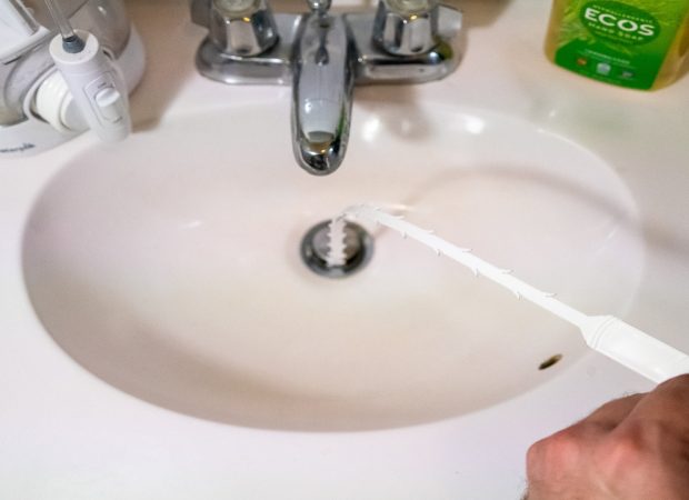 Plumber clearing a blocked bathroom sink drain with a drain snake tool in Brisbane