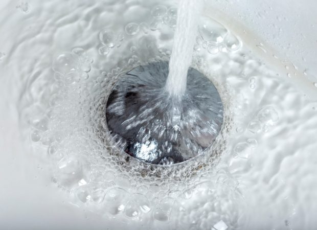 Water flowing down a bathroom sink drain with visible bubbles and running tap water
