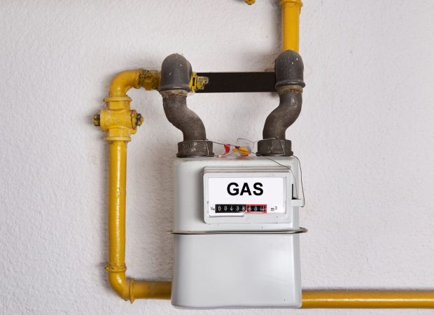 Close-up of a gas meter attached to yellow gas pipes on a wall, displaying the gas usage readings.