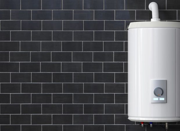 Modern white water heater installed on a dark tiled wall, with visible temperature controls and pipes.