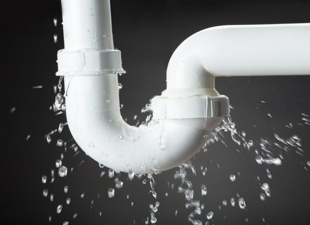 A leaking PVC pipe with water spraying out from a joint.