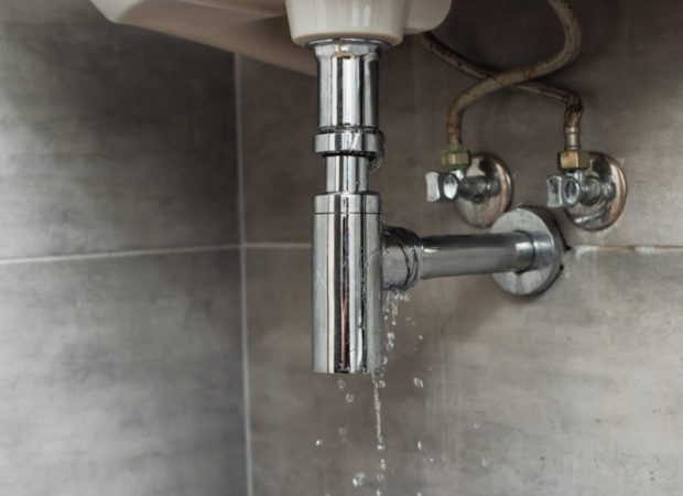 Leaking bathroom sink pipe and drain trap with water dripping underneath the basin