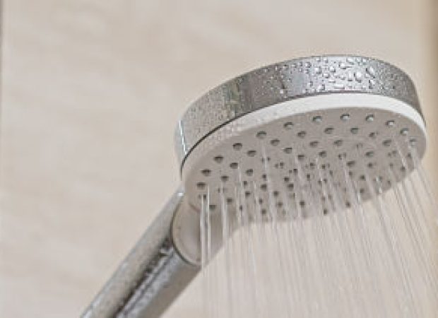 Shower head running with water spraying evenly in a bathroom